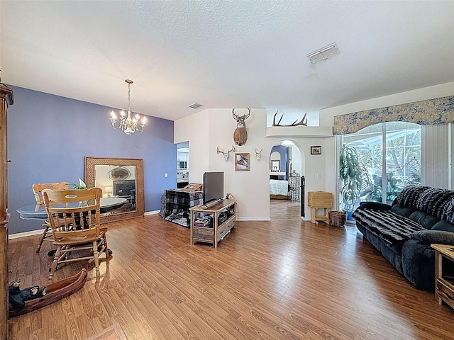 living room with a notable chandelier, visible vents, light wood-style flooring, baseboards, and arched walkways