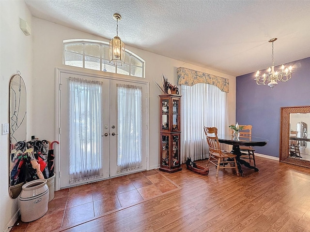 foyer with a wealth of natural light, french doors, wood finished floors, and a notable chandelier