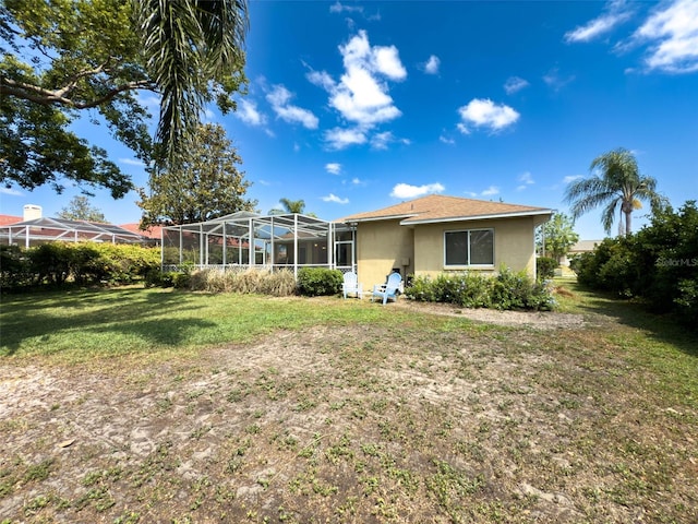rear view of property featuring stucco siding, a yard, and glass enclosure