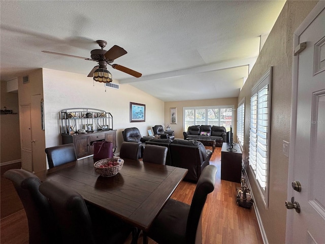 dining room with light wood-style flooring, visible vents, vaulted ceiling, and a textured ceiling