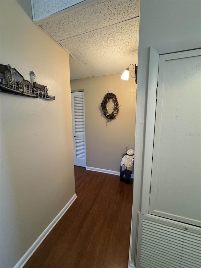 hallway with dark wood-style floors, a drop ceiling, and baseboards