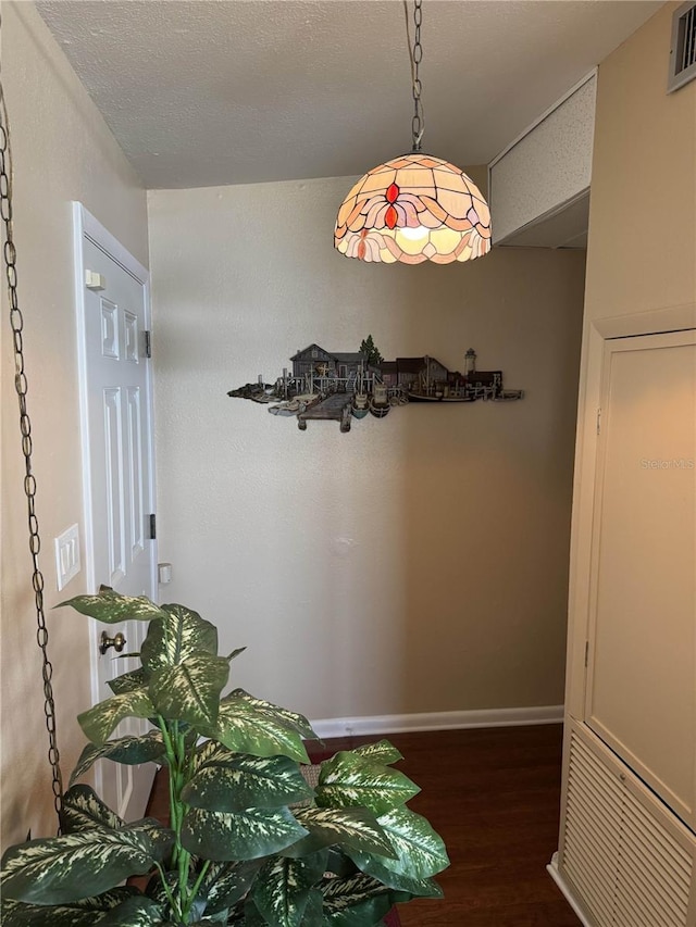 hallway with a textured ceiling, wood finished floors, visible vents, and baseboards