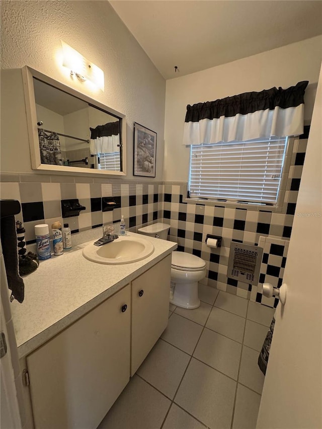 bathroom featuring toilet, a wainscoted wall, tile patterned flooring, vanity, and tile walls