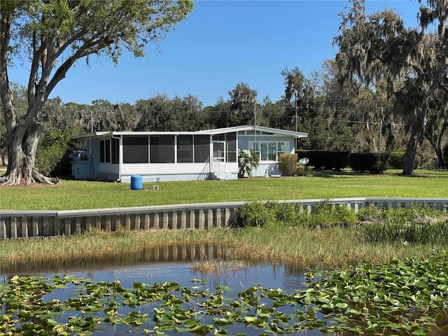 rear view of property with a sunroom, a water view, and a lawn