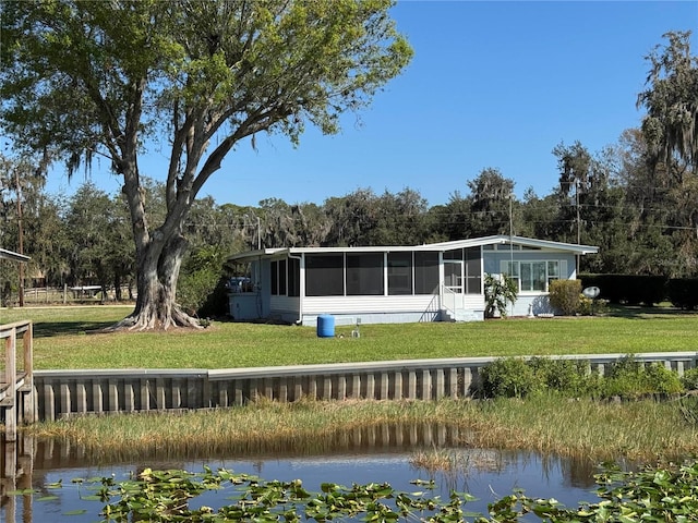 back of house with a sunroom, a water view, and a lawn