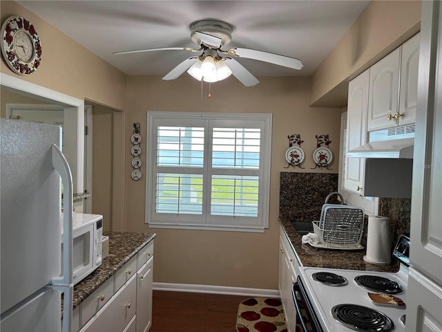 kitchen with white cabinets, dark stone countertops, white appliances, under cabinet range hood, and baseboards