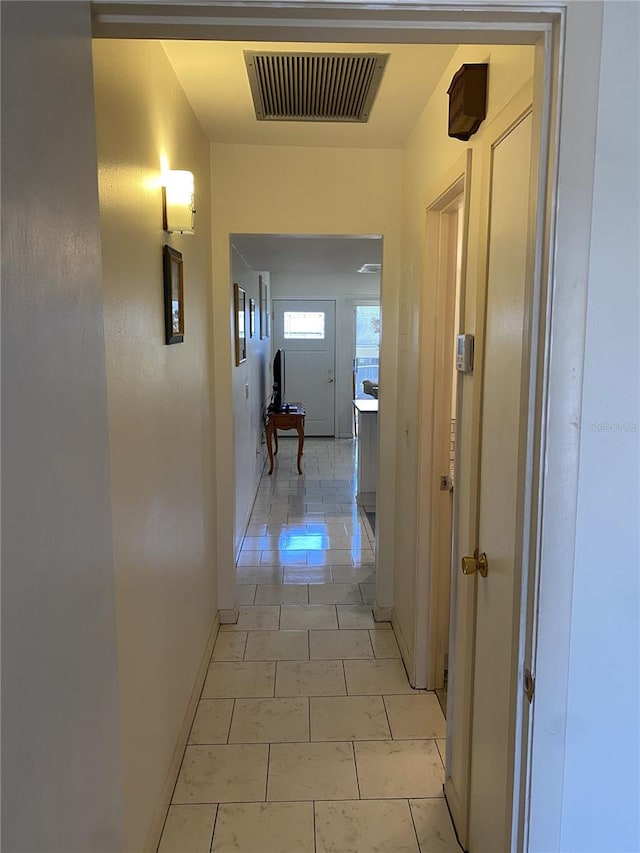 hallway with light tile patterned flooring, visible vents, and baseboards