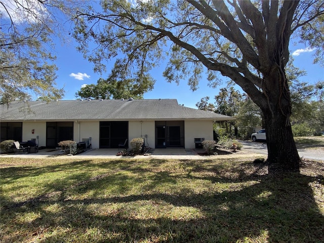 rear view of house with stucco siding, a patio, and a yard