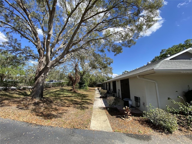 view of property exterior featuring roof with shingles, cooling unit, and stucco siding