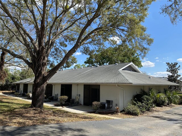 view of side of property featuring a shingled roof, central AC unit, and stucco siding