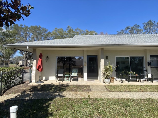 back of property with a patio area, a shingled roof, fence, and stucco siding