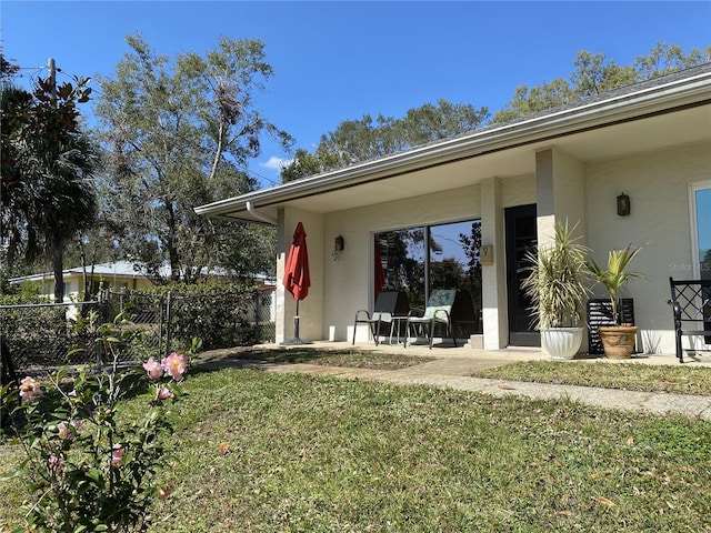 view of exterior entry with a lawn, a patio area, fence, and stucco siding