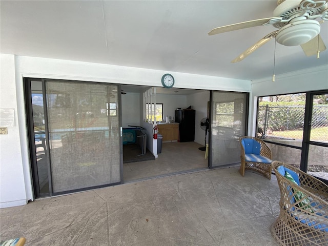 unfurnished sunroom featuring a wood stove, a wealth of natural light, and a ceiling fan