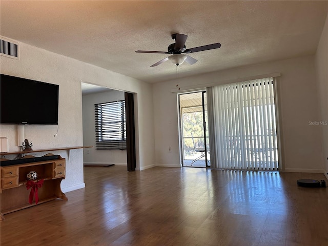 living area featuring a wealth of natural light, visible vents, a textured ceiling, and wood finished floors