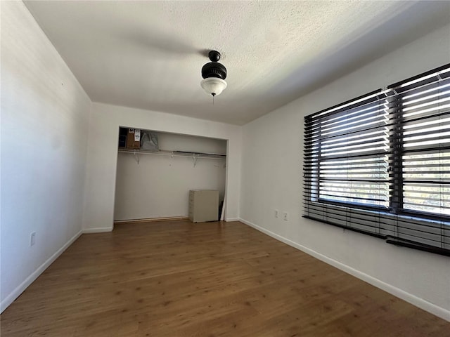 unfurnished bedroom featuring a textured ceiling, wood finished floors, a closet, and baseboards