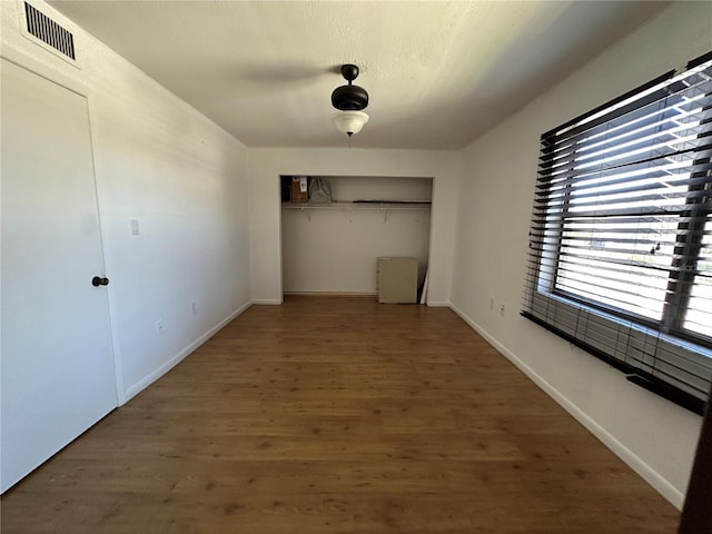 unfurnished bedroom with wood finished floors, visible vents, baseboards, ceiling fan, and a closet