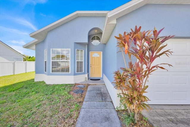 entrance to property featuring a lawn, an attached garage, fence, and stucco siding