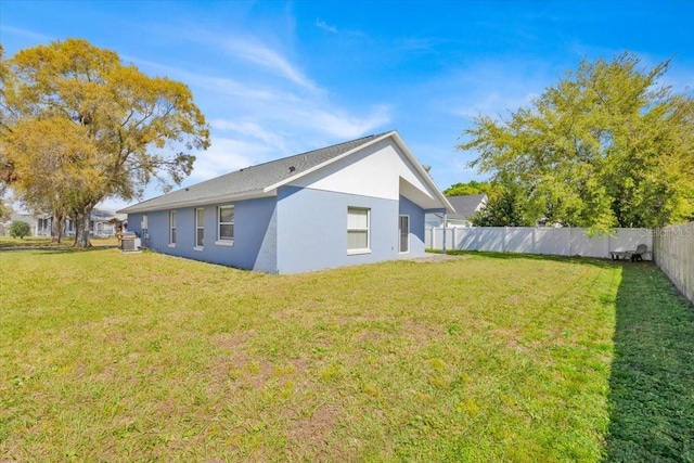 rear view of house with a yard, cooling unit, fence private yard, and stucco siding