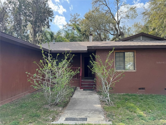 view of exterior entry featuring stucco siding, a yard, roof with shingles, and crawl space