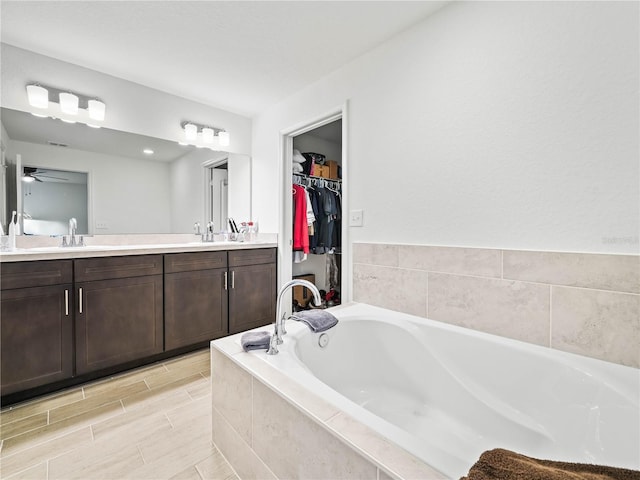 full bath with double vanity, a ceiling fan, a garden tub, and a sink