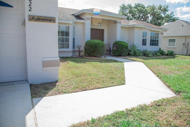 view of front of home featuring a shingled roof, stucco siding, and a front lawn