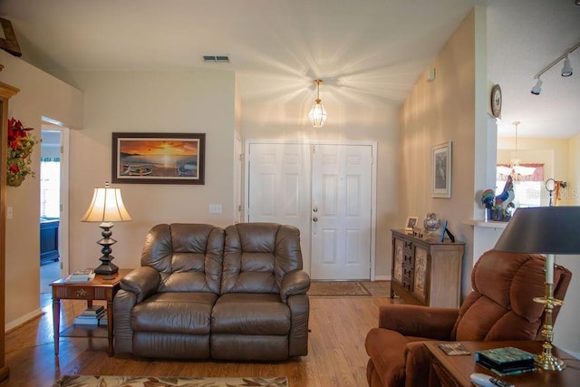 living room featuring visible vents, baseboards, a notable chandelier, wood finished floors, and rail lighting