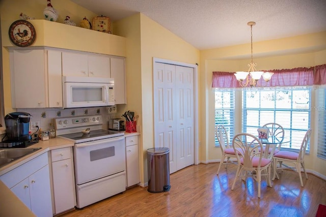 kitchen with an inviting chandelier, white appliances, light wood-style flooring, light countertops, and lofted ceiling