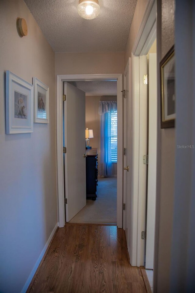 hallway with a textured ceiling, wood finished floors, and baseboards