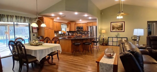 dining area with high vaulted ceiling and light wood-style flooring