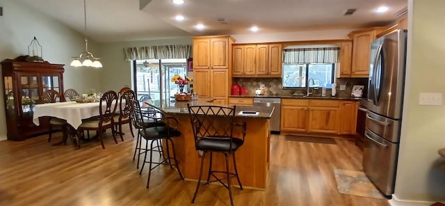 kitchen with light wood finished floors, stainless steel appliances, a kitchen bar, and plenty of natural light