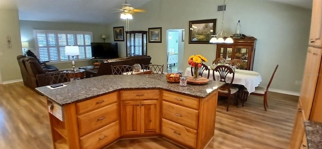 kitchen featuring light wood-type flooring, a ceiling fan, open floor plan, and dark stone countertops