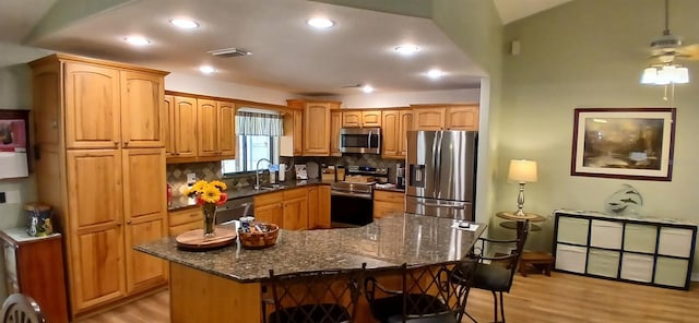 kitchen with dark stone countertops, a sink, decorative backsplash, stainless steel appliances, and light wood finished floors