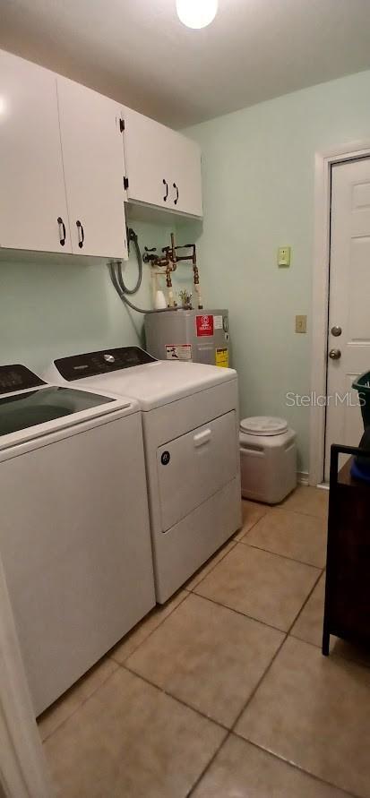 washroom with washing machine and dryer, water heater, cabinet space, and light tile patterned floors