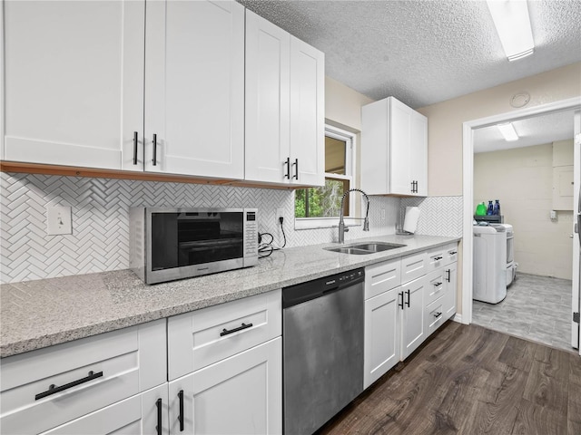 kitchen with dark wood finished floors, dishwasher, a sink, white cabinets, and washer and dryer