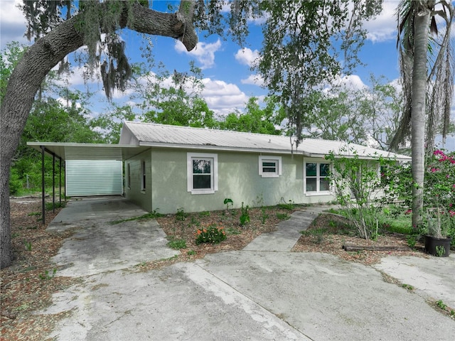 ranch-style house featuring a carport, stucco siding, driveway, and metal roof