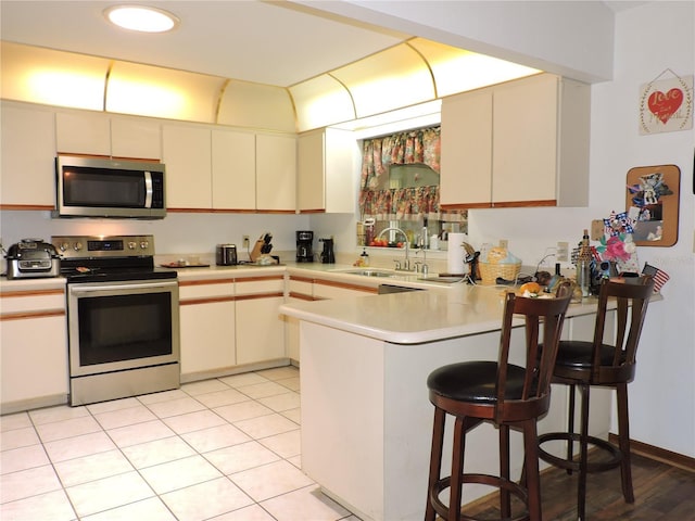 kitchen featuring appliances with stainless steel finishes, a sink, light countertops, a kitchen breakfast bar, and a peninsula