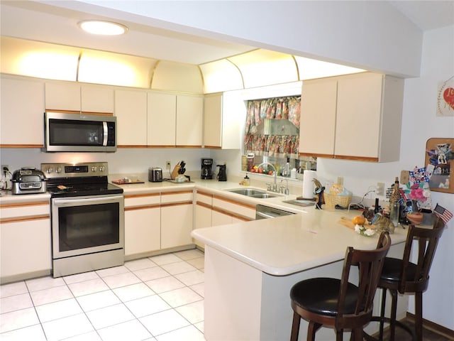 kitchen featuring a peninsula, a kitchen breakfast bar, light countertops, a sink, and appliances with stainless steel finishes