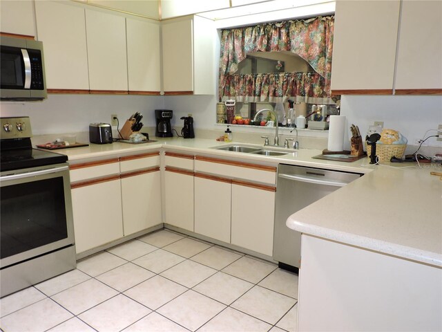 kitchen featuring light countertops, cream cabinetry, a sink, light tile patterned floors, and stainless steel appliances