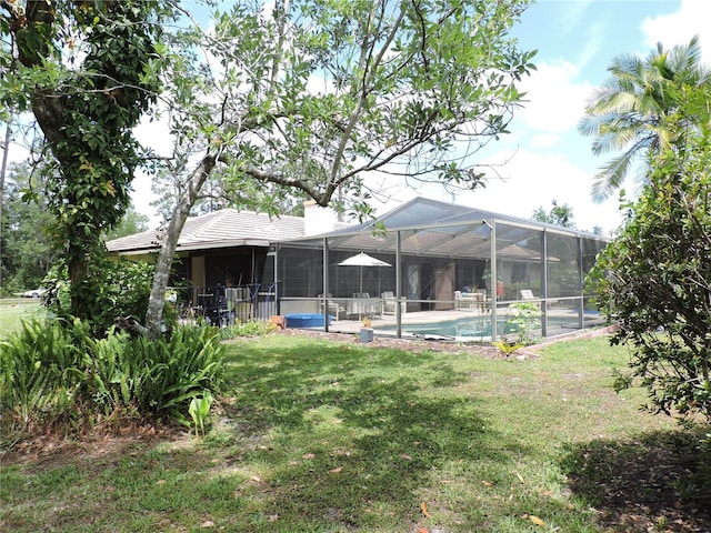 rear view of house featuring glass enclosure, a chimney, a yard, and an outdoor pool