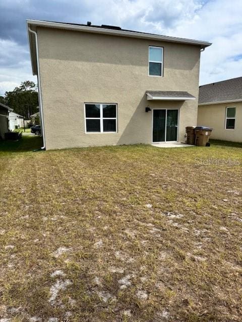back of property with stucco siding and a lawn