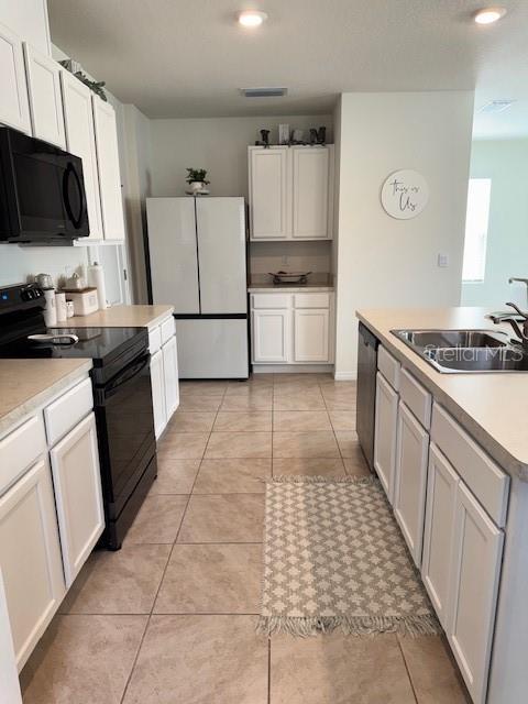 kitchen with black appliances, a sink, light countertops, light tile patterned floors, and white cabinets