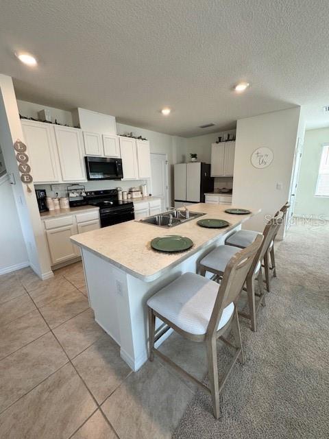 kitchen featuring a sink, black appliances, light countertops, white cabinets, and a center island