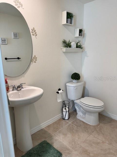 half bath featuring toilet, baseboards, and tile patterned floors