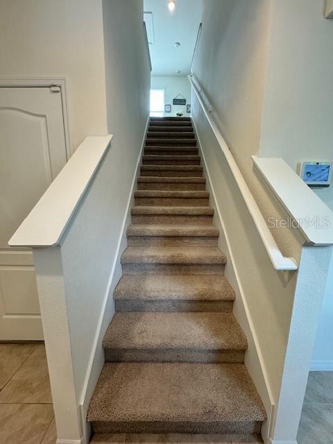 stairway with baseboards, tile patterned flooring, and carpet