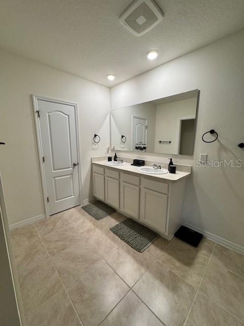 full bath featuring double vanity, a textured ceiling, baseboards, and tile patterned floors