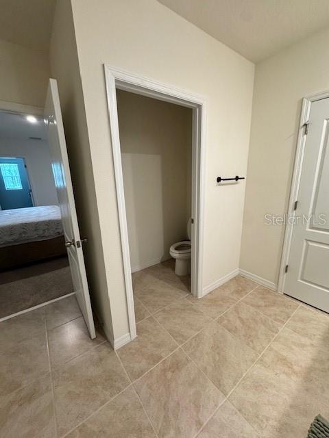 ensuite bathroom with tile patterned floors, baseboards, and toilet