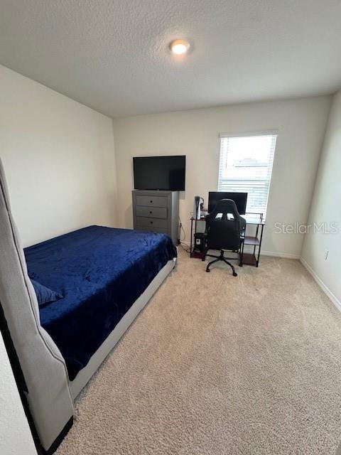 bedroom with light colored carpet, a textured ceiling, a desk, and baseboards