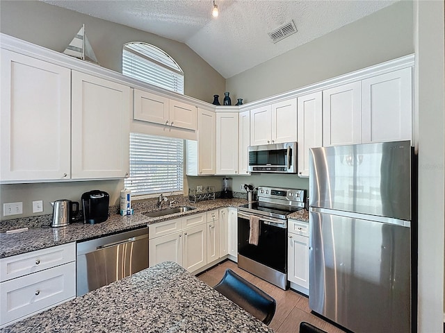 2696 Hemingway Ave, Haines City, FL 33844 - kitchen with stainless steel appliances, lofted ceiling, white cabinetry, a textured ceiling, and dark stone counters