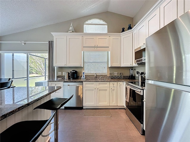 2696 Hemingway Ave, Haines City, FL 33844 - kitchen featuring appliances with stainless steel finishes, lofted ceiling, healthy amount of natural light, white cabinetry, and dark stone countertops