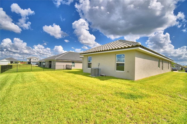 rear view of property with central air condition unit and a lawn